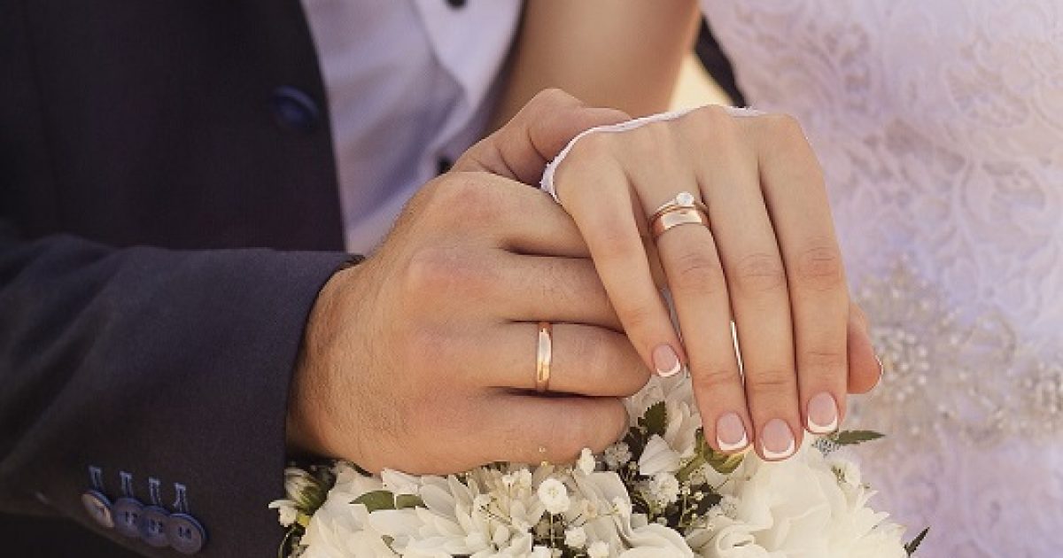 A closeup shot of newlyweds holding hands and showing the wedding rings